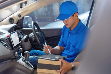 Happy young delivery man using tablet in van with carton box parcels on seat. Delivery service courier concept