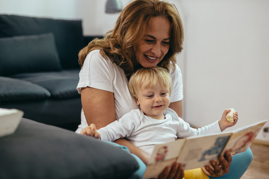 baby boy with his grandmother at home reading picture book