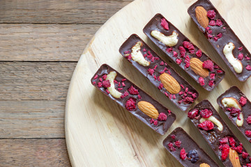 Top view of delicious raw foods dessert from natural chocolate, cashew, almond and raspberry. Sweet sticks lay on round kitchen board on wooden background with copy space. Dietary tea treat.