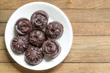 Homemade chocolate candies. Delicious raw vegan sweets, sprinkled with coconut flakes. Top view of natural harmless dessert on white saucer on wooden table.