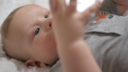 Cute baby holds phone in hands. The child plays with cell phone, examines it, tugs in his hands and tries to eat smartphone putting it in his mouth