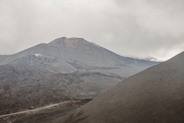 Top of crater Mount Etna volcano, frozen cold lava smokes, thick clouds