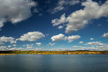Beautiful autumn landscape panorama with forest by a lake with clouds above it.