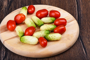 Fresh ripe little cucumbers and cherry tomatoes on a wooden cutting board.