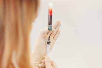 Scientist hand holding test tube with blood in laboratory on blurred background. Portrait of a beautiful female chemist looking analyzing a blood test tube in a medical cabinet