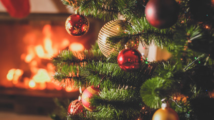 Closeup toned image of colorful baubles on Christmas tree against burning fire in fireplace