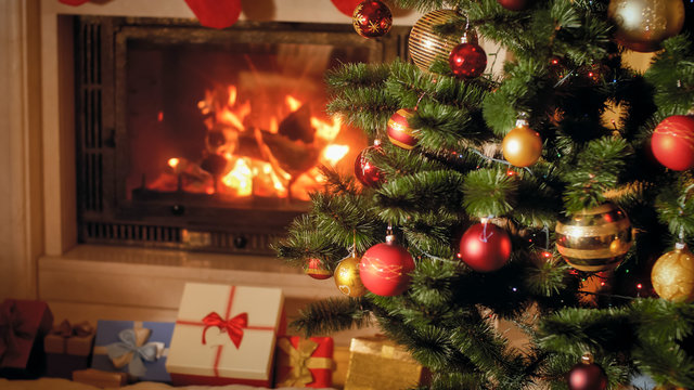 Closeup image of big stack of Christmas gifts and presents next to burning fireplace and decorated Xmas tree