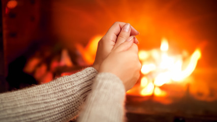 Closeup photo of young wooman feeling cold sitting by the burning fire at house and rubbing...