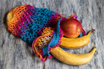 Ecological cotton mesh for carrying and storing products. Durable, bright. Fruits lie in and near her. Apples and yellow bananas. View from above. On a bright background. Copy space. 