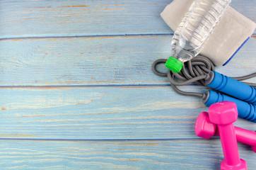 Top or flat lay view of dumbbells, towel, water and skipping rope with copy space area on blue wooden background. Healthy concept. Selective focus.