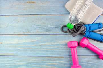 Top or flat lay view of dumbbells, towel, water and skipping rope with copy space area on blue wooden background. Healthy concept. Selective focus.