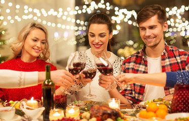holidays and celebration concept - happy friends having christmas dinner at home, drinking red wine...