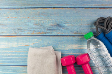 Top or flat lay view of dumbbells, towel, water and skipping rope with copy space area on blue wooden background. Healthy concept. Selective focus.