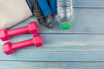 Top or flat lay view of dumbbells, towel, water and skipping rope with copy space area on blue wooden background. Healthy concept. Selective focus.