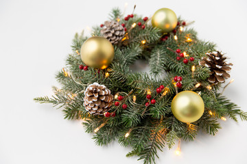 Obraz na płótnie Canvas winter holidays, new year and decorations concept - wreath of fir branches with golden balls, pine cones and garland lights on white background