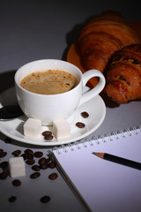 A Cup of coffee, croissants and a notebook on a dark background
