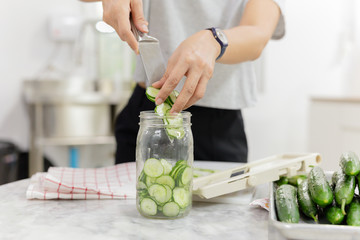 Woman hands with knife putting cucumber into glass jar in kitchen table.