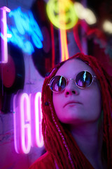 Girl in neon lights, beautiful woman in sunglasses, with pink hair, with dreadlocks pigtails, bright and stylish in glow of neon signs