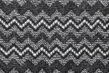 Background in the form of a woolen product with a pattern of two white and three black horizontal zigzags on a gray background