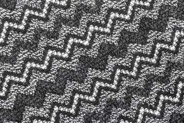 Background in the form of a woolen product with a pattern of alternating diagonal black and white zigzags