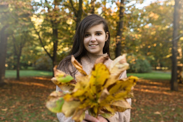Fototapeta na wymiar Uśmiechnięta dziewczyna trzyma liście w rękach.