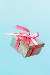 Gold color gift box with pink ribbon on blue background close-up, copy space. Levitation