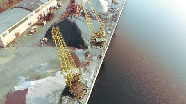 port cranes on the river bank produce sand. Port cranes with a bucket on the river bank. Extraction of river sand. Port cargo cranes extracts river sand, production. Sunset. Barge.