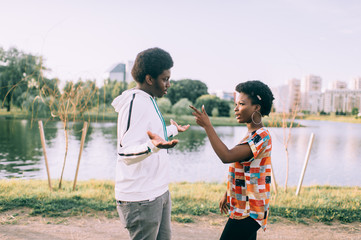 Serious African American girl blaming upset man, pointing finger at him, strict sister talking with brother, standing  together outdoor, couple talking about relationships, break up concept.