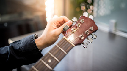 Male hand guitarist adjusting pegs on acoustic guitar during music lesson at home. String musical instrument concept - obrazy, fototapety, plakaty