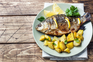 Baked fish carp with lemon greens and potatoes on a plate. Wooden background. Copy space