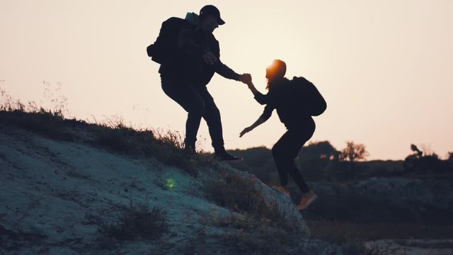 Couple hiking help each other silhouette in mountains. Teamwork couple hiking, help each other, trust assistance, sunset. Man giving hand a woman to help her to climb the mountain.