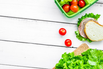 homemade lunch with lettuce, grape and sandwich in green lunchbox top view mockup