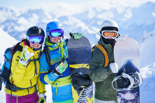 Photo of three happy snowboarders in helmet on background of mountains.