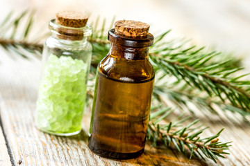 cosmetic spruce oil and salt in bottles with fur branches on wooden table background