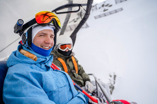 Image of two snowboarders in helmet and mask on cable car .