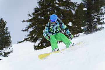 Fototapeta na wymiar Man snowboarder riding on mountainside on background of trees in afternoon