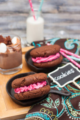 Chocolate sandwich cookies with pink butter cream in black iron mini skillets. Bottle of milk and glass of milkshake with marshmallows on the background.