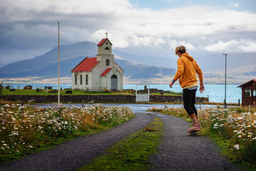 Young skater skateboarding towards a church and a cemetery in Iceland © Nick Fox