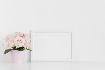 White frame mockup with pink roses in a pot on a white table.Landscape orientation.