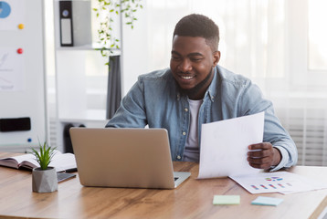 Young black businessman working with laptop and papers in office