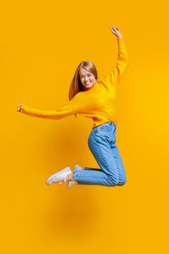 Joyful teen girl jumping in air on orange background