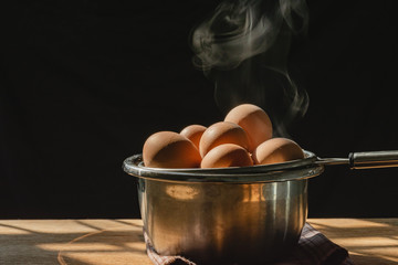 The steam from boiled eggs on the old wood table and black background with morning sun light in the kitchen,Eggs are high-protein foods, children of growing age should eat eggs daily, Selective focus.