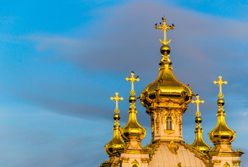 Fototapeta na wymiar Golden domes of a Christian Church in Peterhof, illuminated by the rays of the setting sun on the background of blue sky.