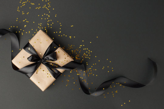 Gift or present box and gold stars confetti on black table top view. Flat lay composition for birthday, mother day, black friday sale, xmas, christmas, new yaer or wedding.