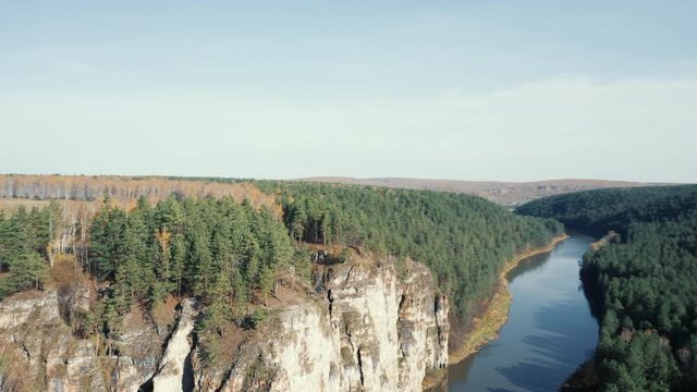 High steep cliffs of curved Ural river Ay; natural landscape with mixed forest on riversides; autumn colored orange yellow birches; aerial view, drone flying over tree crones; bright fall season day