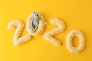 Happy New Year 2020. Number 2020 knitted from yarn and gray toy mouse symbol of year on bright yellow background, cheese color. Flat lay, top view, copy space