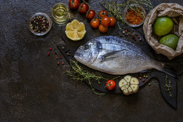 Dorado fish with greens thyme and rosemary and fresh vegetables on a dark background
