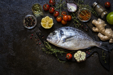 Dorado fish with greens thyme and rosemary and fresh vegetables on a dark background
