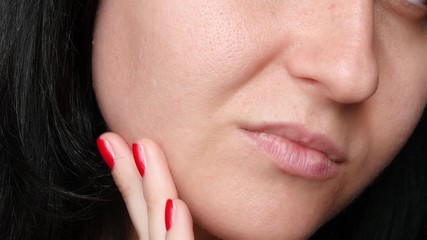 Obraz premium Female face close-up. Skin texture with enlarged pores. The girl touches the fingers of the problem skin of the face, considering it. The concept of care for problem skin, age-related changes and the
