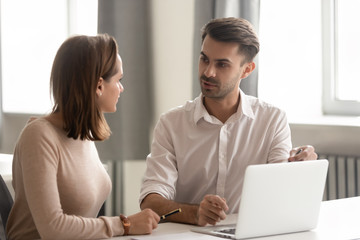 Serious businessman mentor teaching new female employee, using laptop